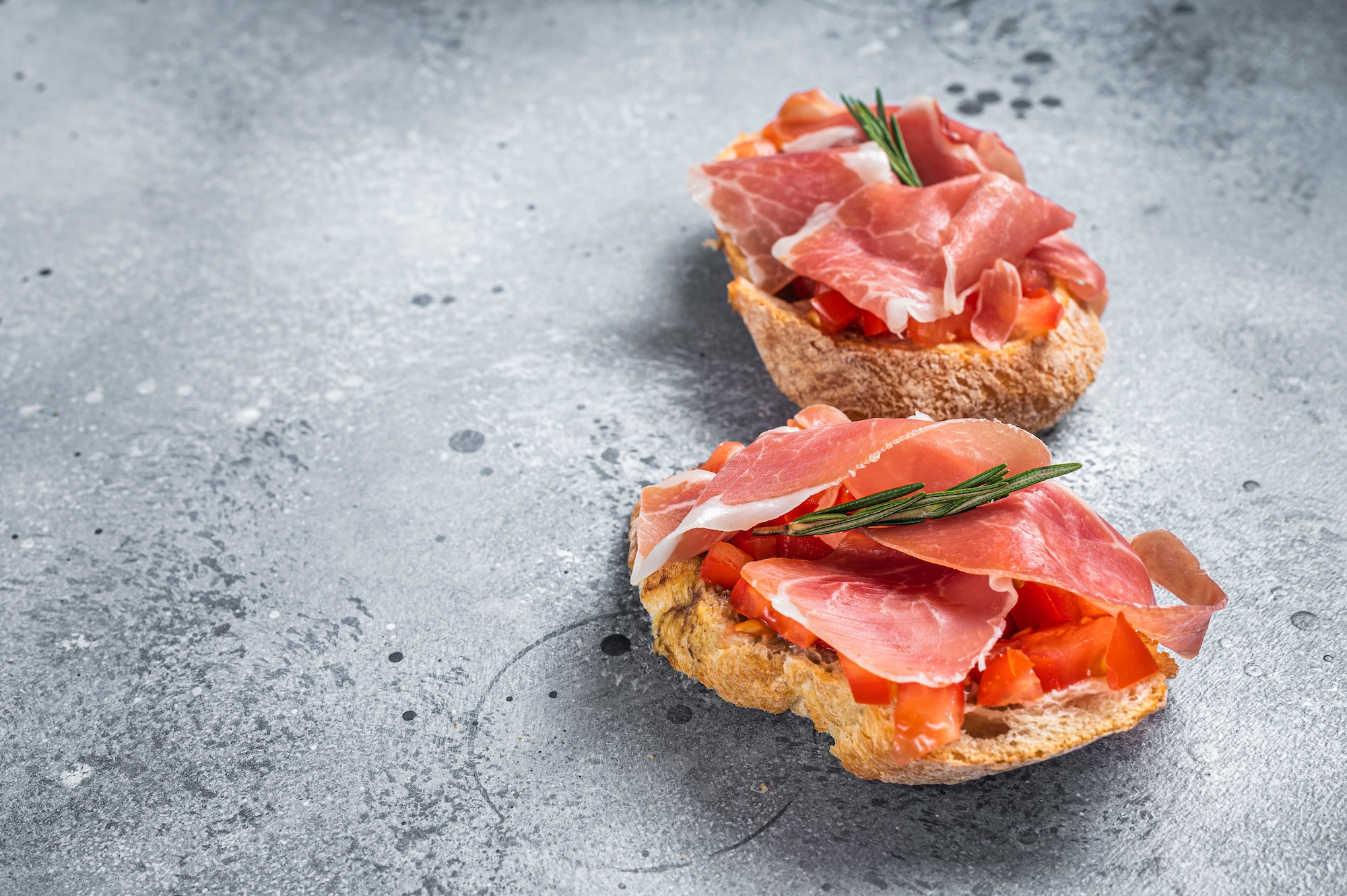 Spanish Tapas with tomatoes and cured Slices of jamon iberico ham, fresh toasts. Gray background